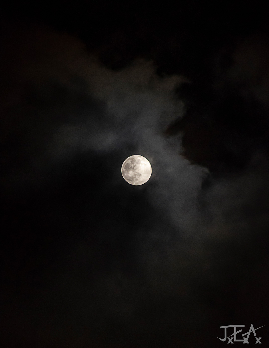 The moon sits full in center frame, illuminating some light clouds against a pitch black sky.