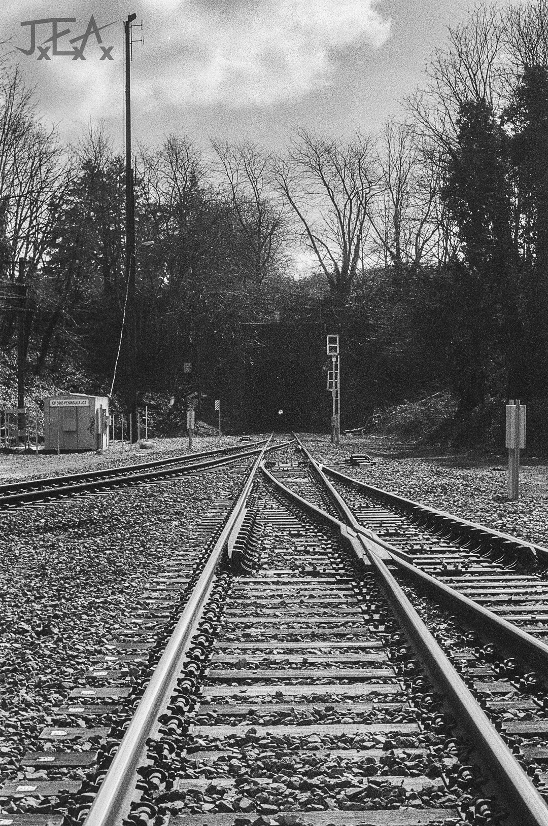 A black and white photo of three sets of train tracks leading into a one track tunnel.